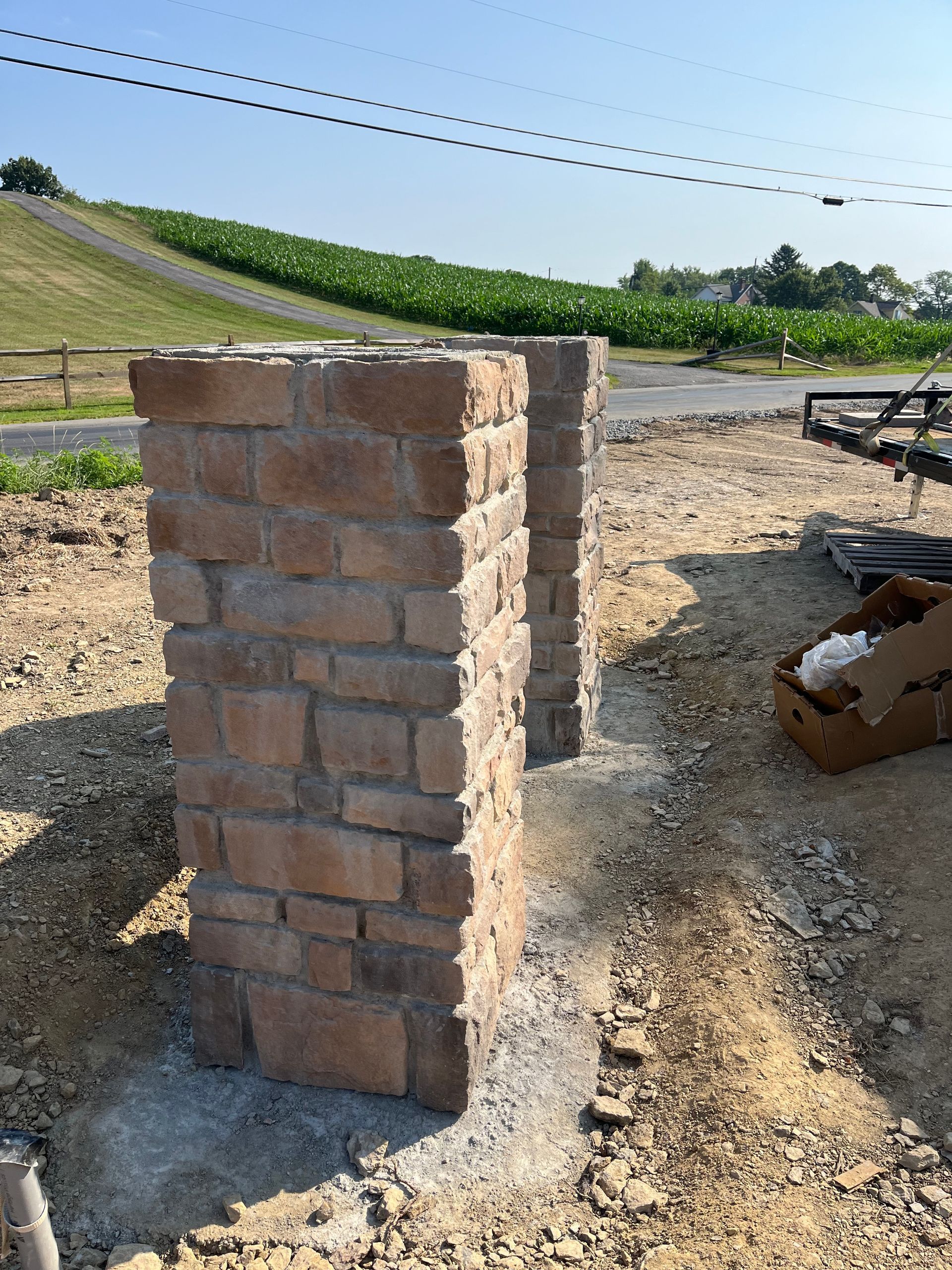 Two brick pillars are being built in a dirt field.