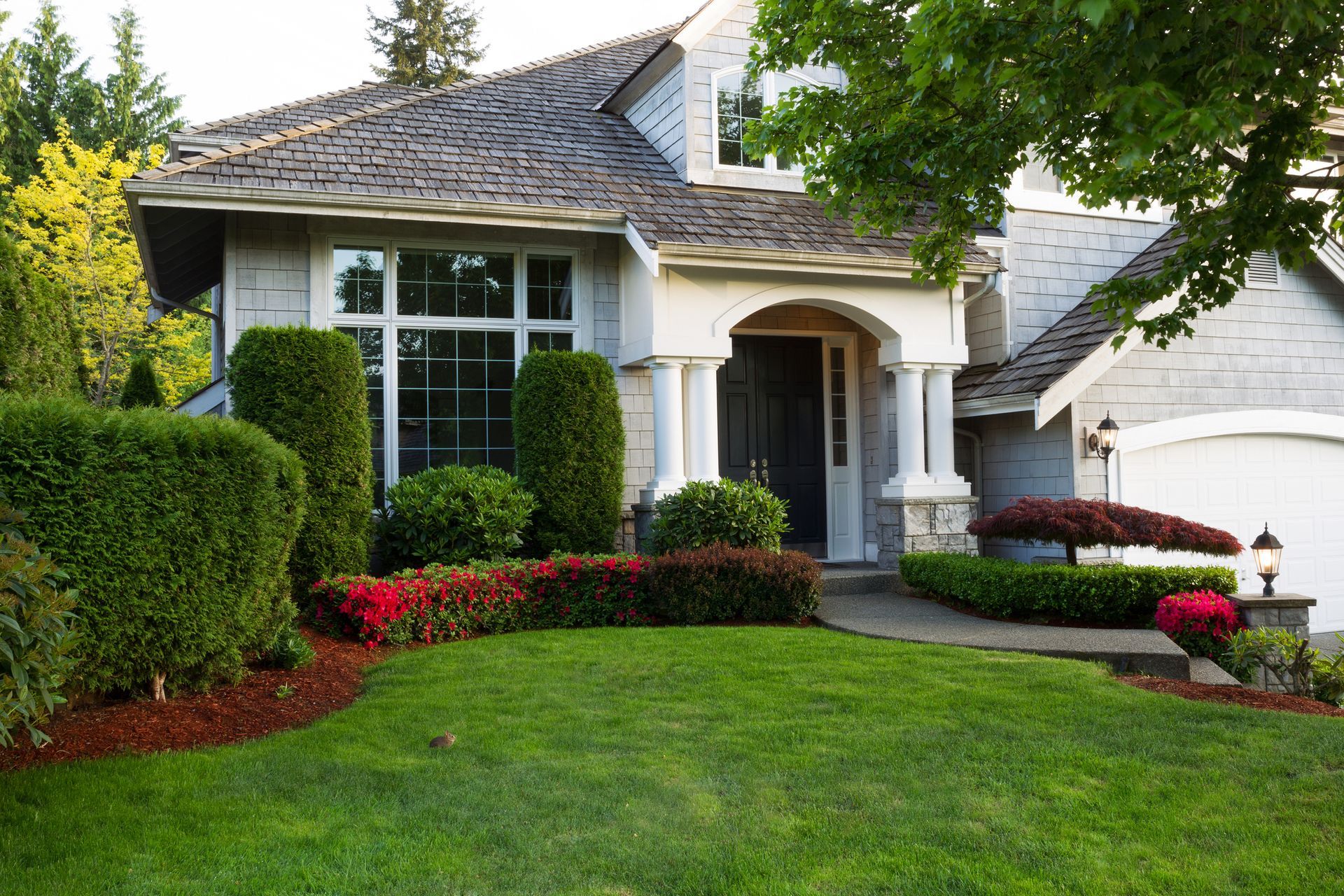 A house with a lush green lawn and bushes in front of it.