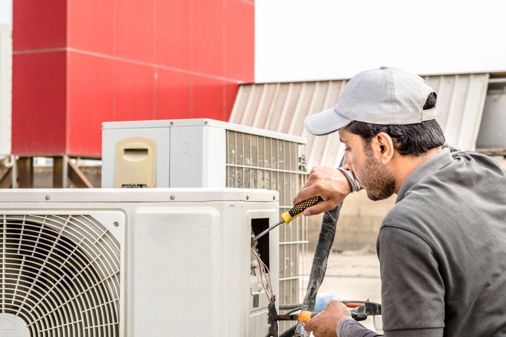 A Man Is Fixing An Air Conditioner With A Screwdriver — Jordan Wheatland Air Conditioning & Refrigeration In Dubbo, NSW