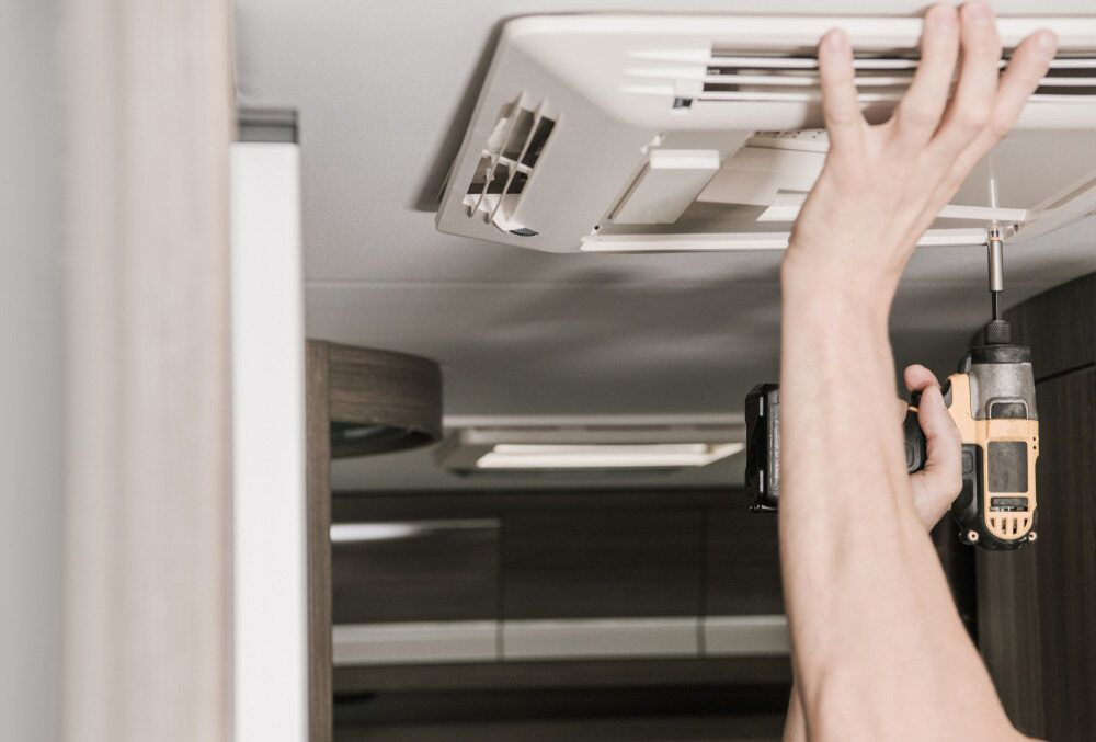 A Person Is Fixing A Ceiling Fan With A Drill — Jordan Wheatland Air Conditioning & Refrigeration In Dubbo, NSW