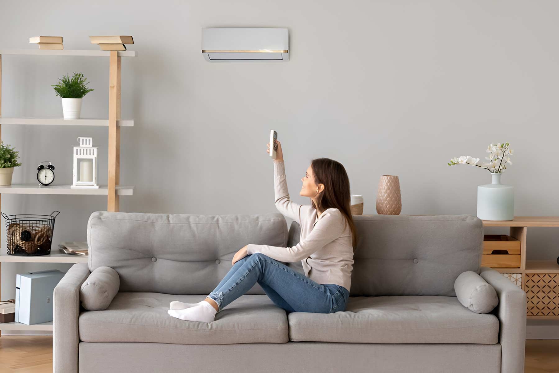 A Woman Is Sitting On A Couch Holding A Remote Control — Jordan Wheatland Air Conditioning & Refrigeration In Wellington, NSW