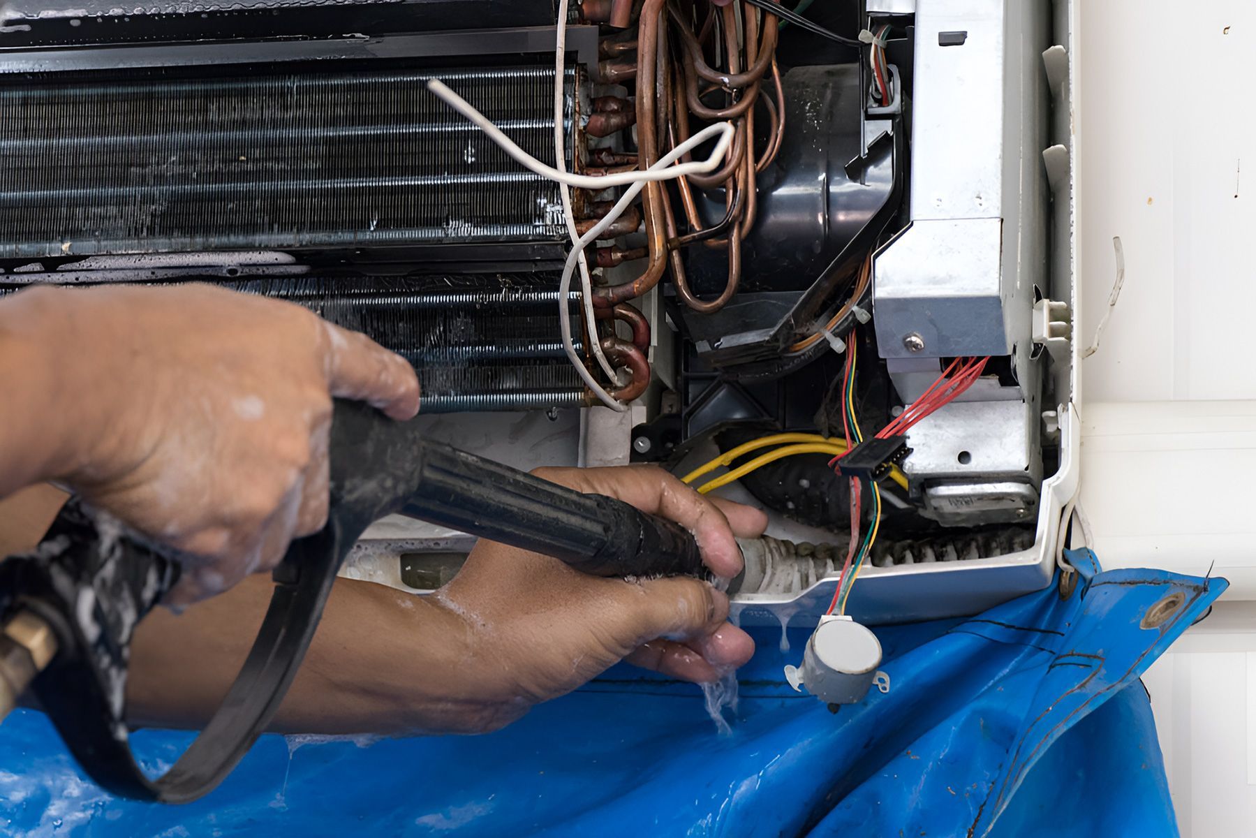 A person is cleaning a refrigerator with a pressure washer — Jordan Wheatland Air Conditioning & Refrigeration In Dubbo, NSW