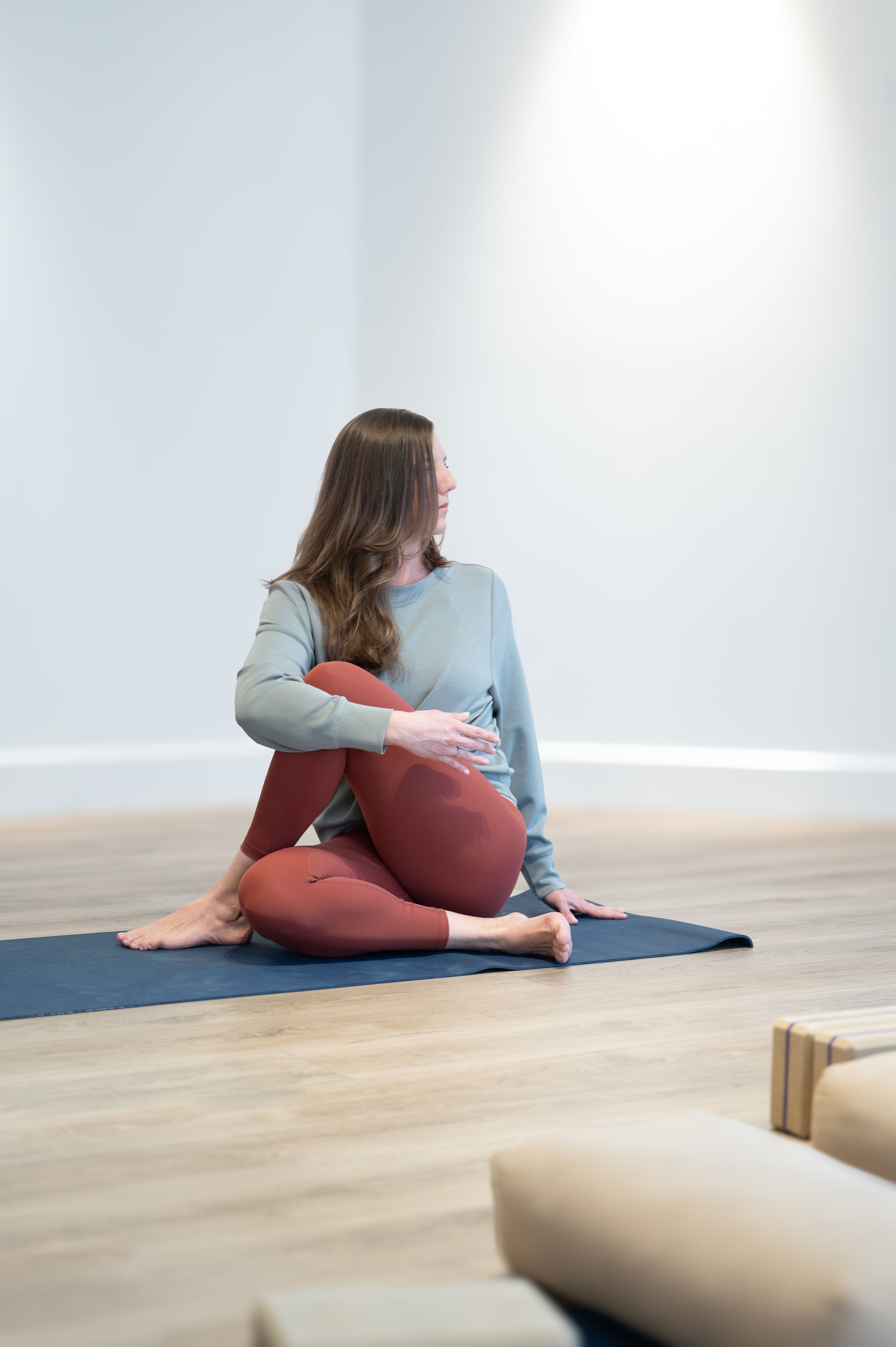 Femme en posture de yoga torsadée, assise sur un tapis, regardant sur le côté.