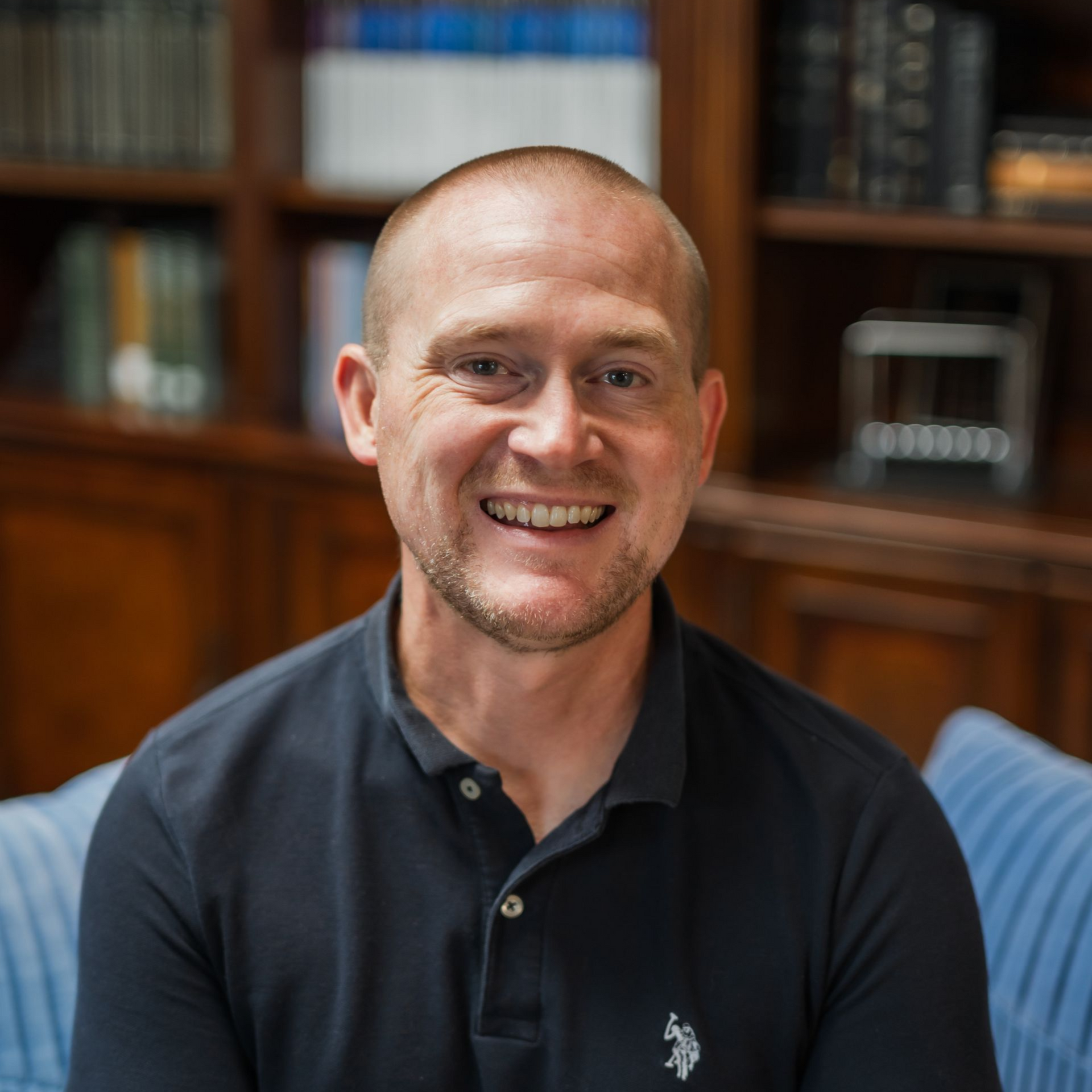 A man in a white shirt is sitting in front of a bookshelf.
