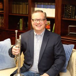 A man in a suit is sitting on a couch holding a trumpet