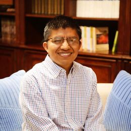A man wearing glasses is smiling while sitting on a couch