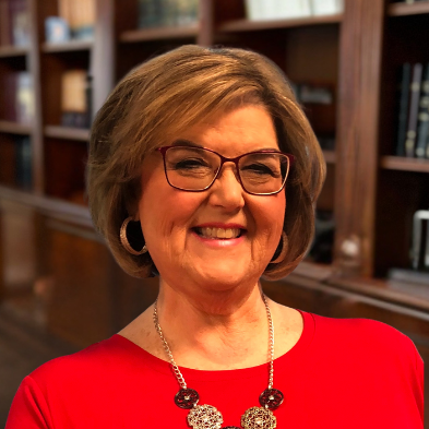 A woman wearing glasses and a red shirt is smiling in front of a bookshelf.