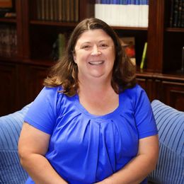 A woman in a blue shirt is sitting on a blue couch and smiling