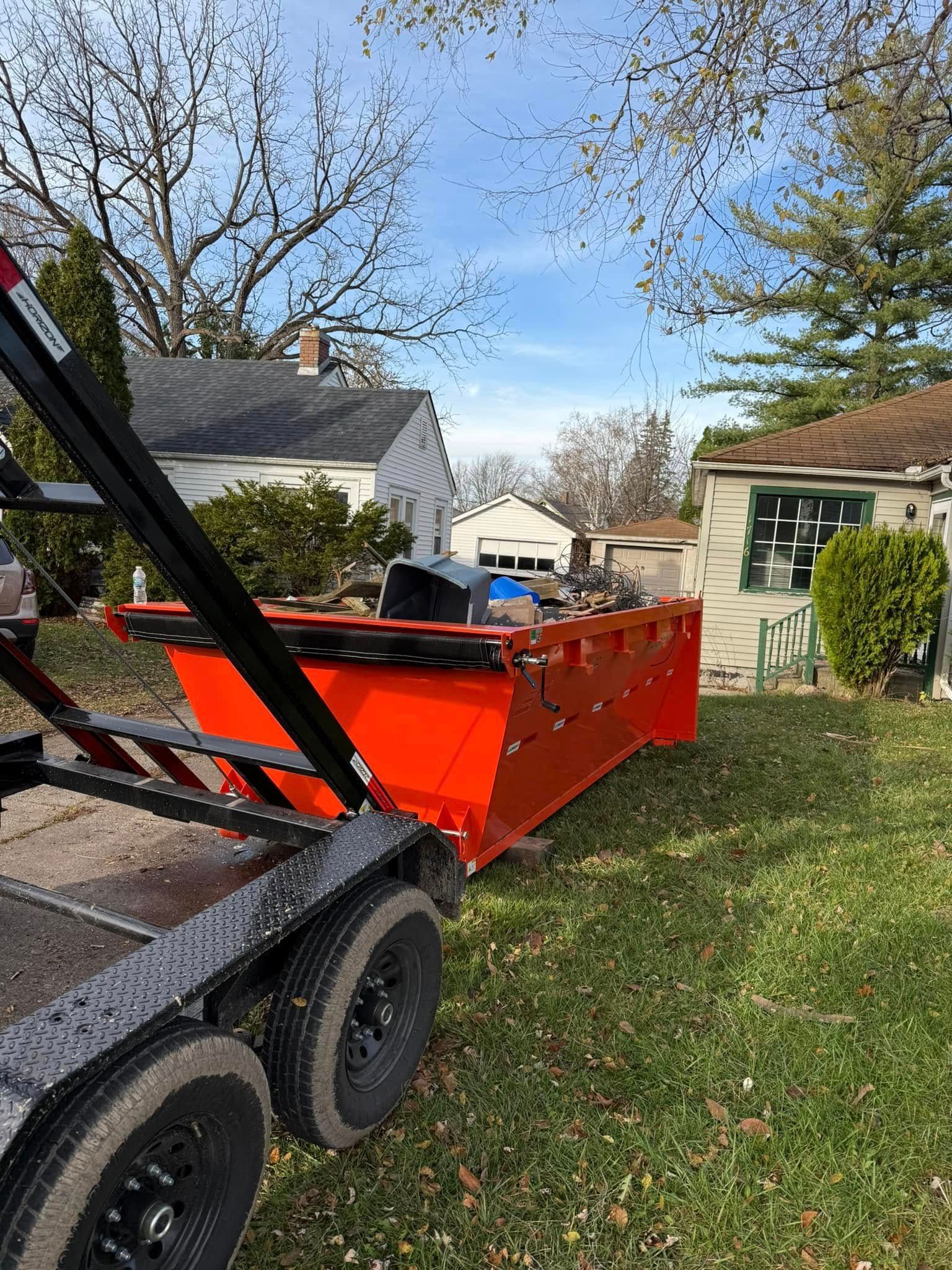 Orange industrial debris bucket on a trailer in a grassy yard, houses in the background.