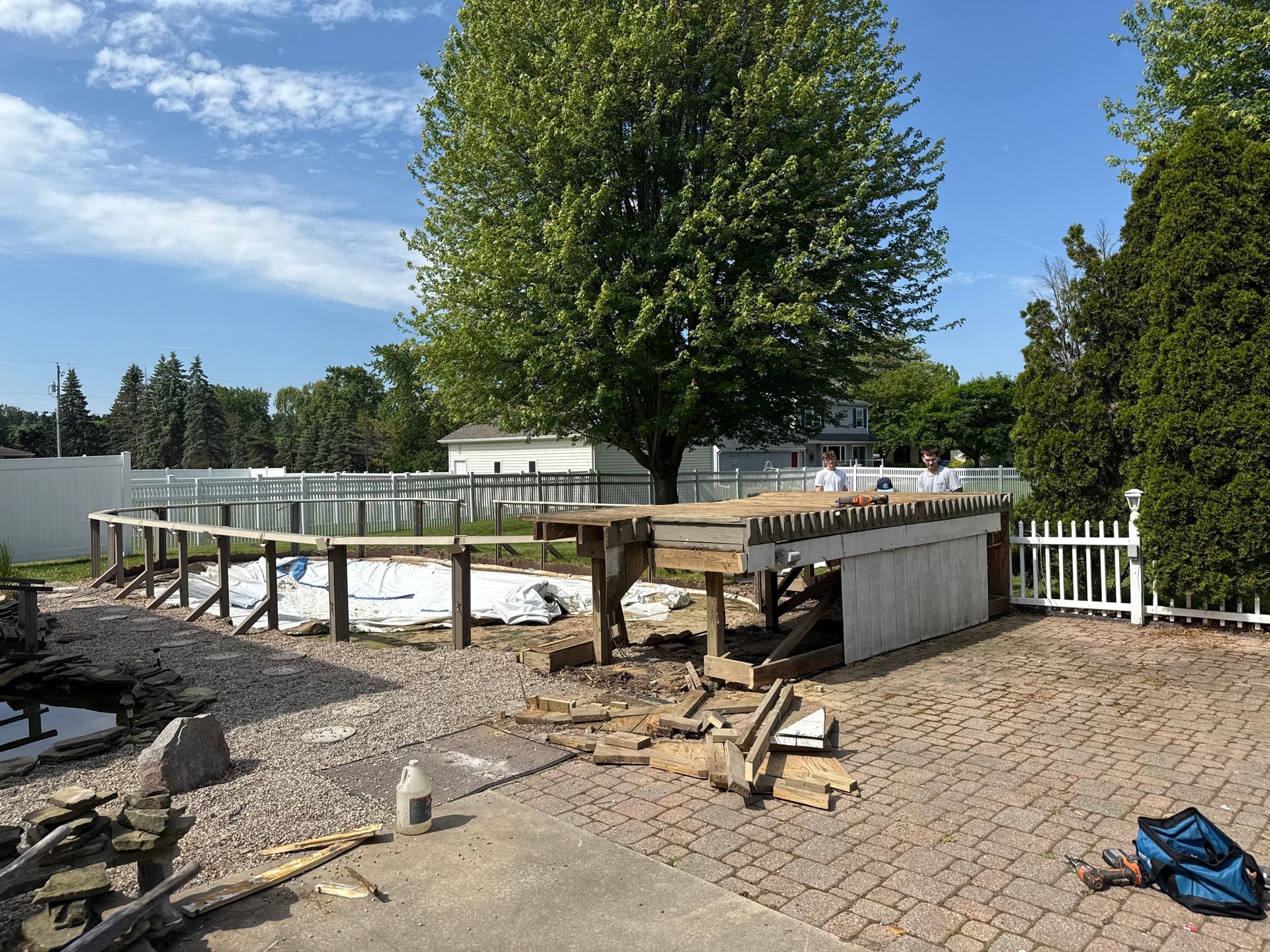 Pool demolition in progress; wood, debris, and partial pool frame on a brick patio.