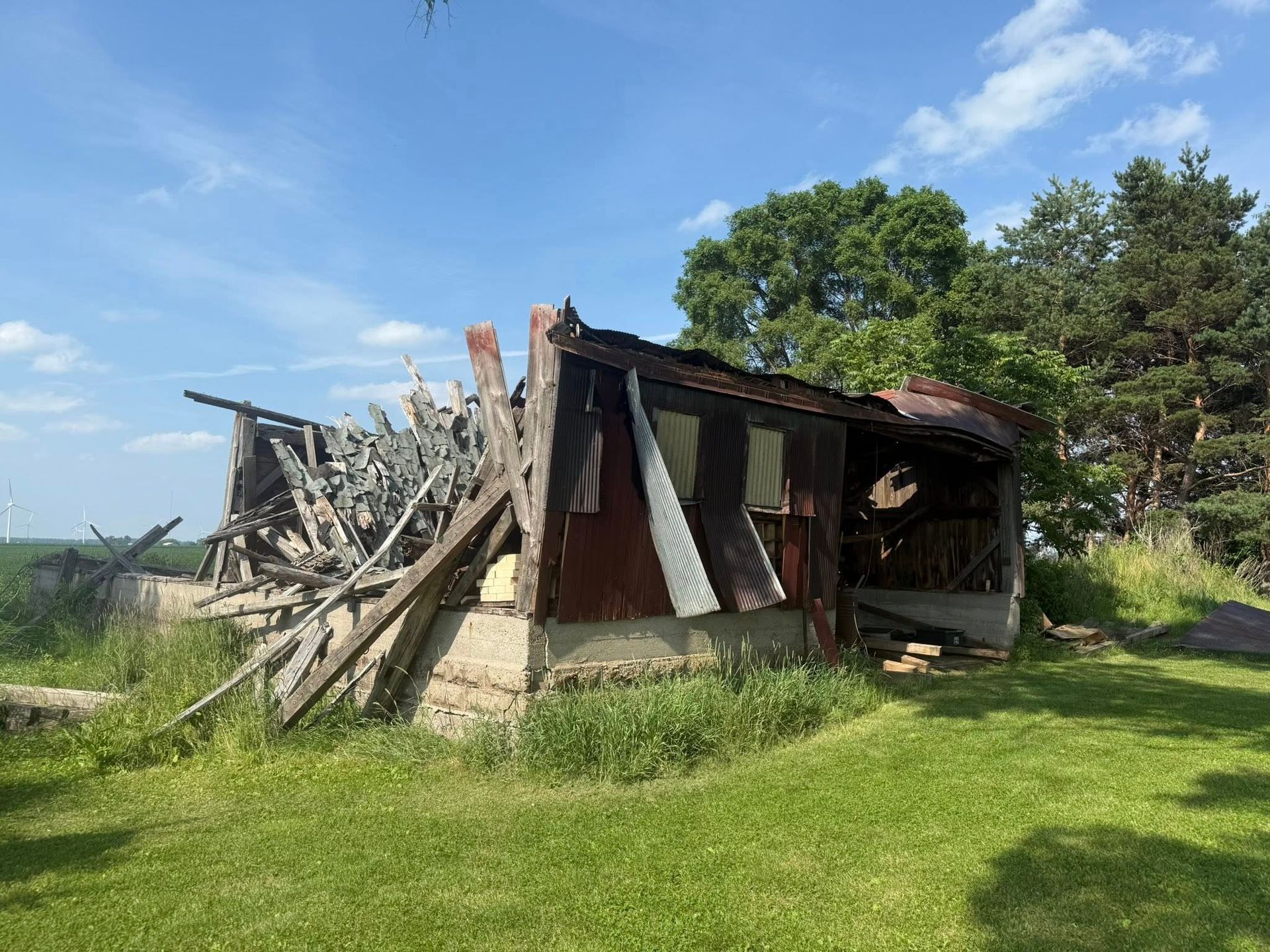 Dilapidated shed in a grassy field under a blue sky, walls and roof partially collapsed.