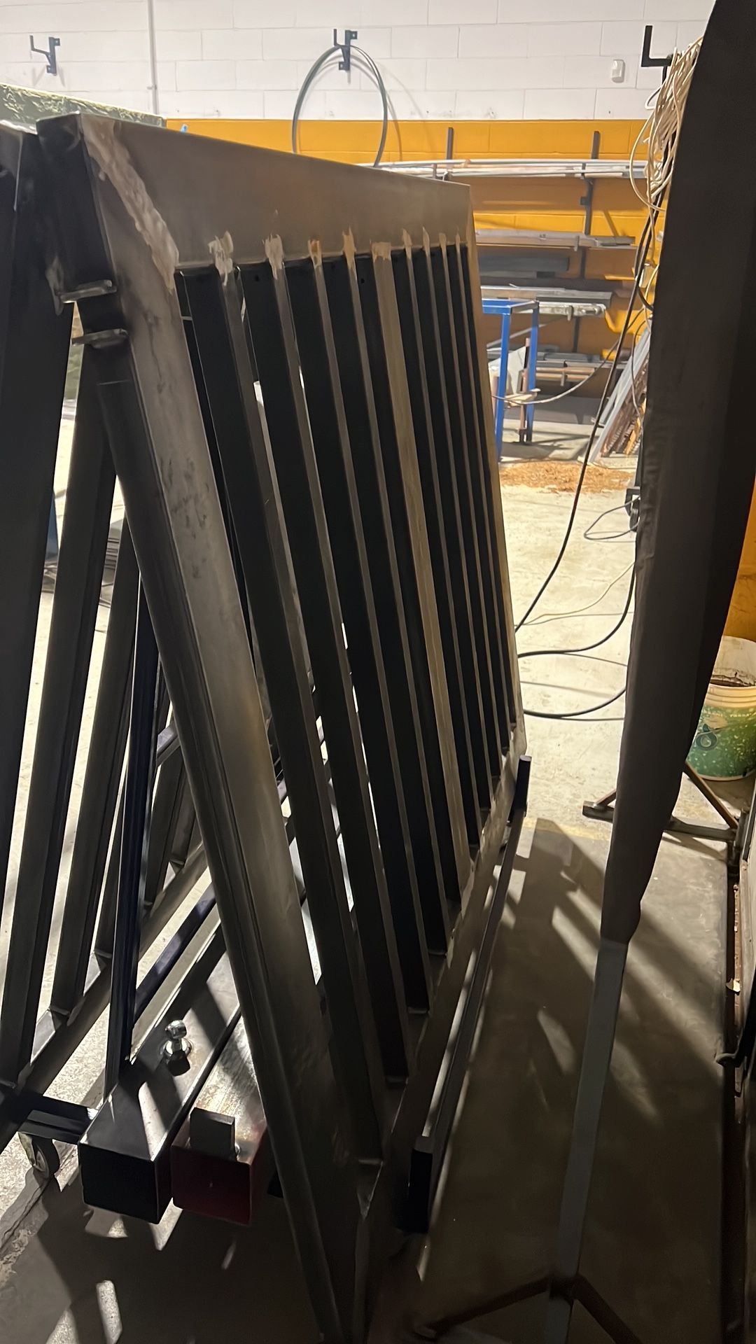 Telai in metallo nero appoggiati in un corridoio di un'officina, con scaffalature gialle sullo sfondo.