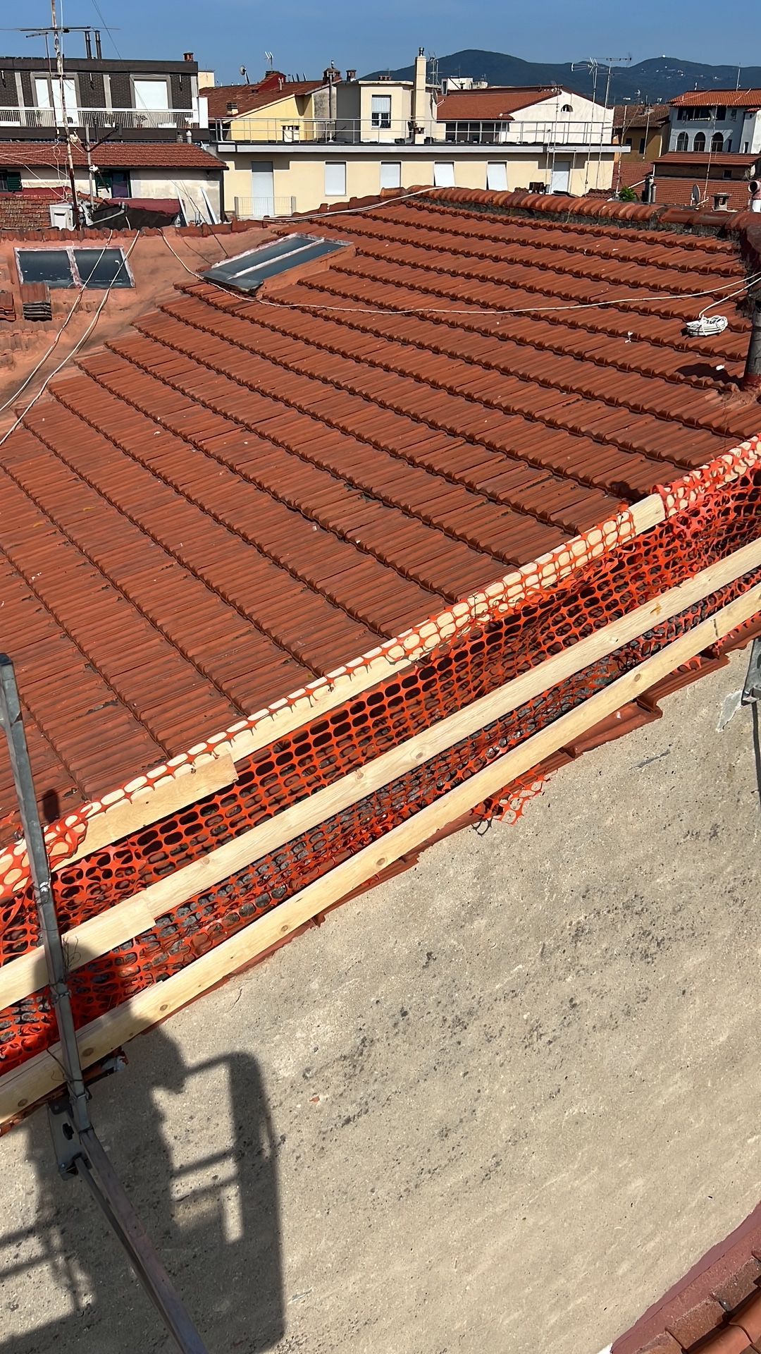 Tetto con tegole di terracotta rossa e lo skyline di una città lontana sotto un cielo limpido