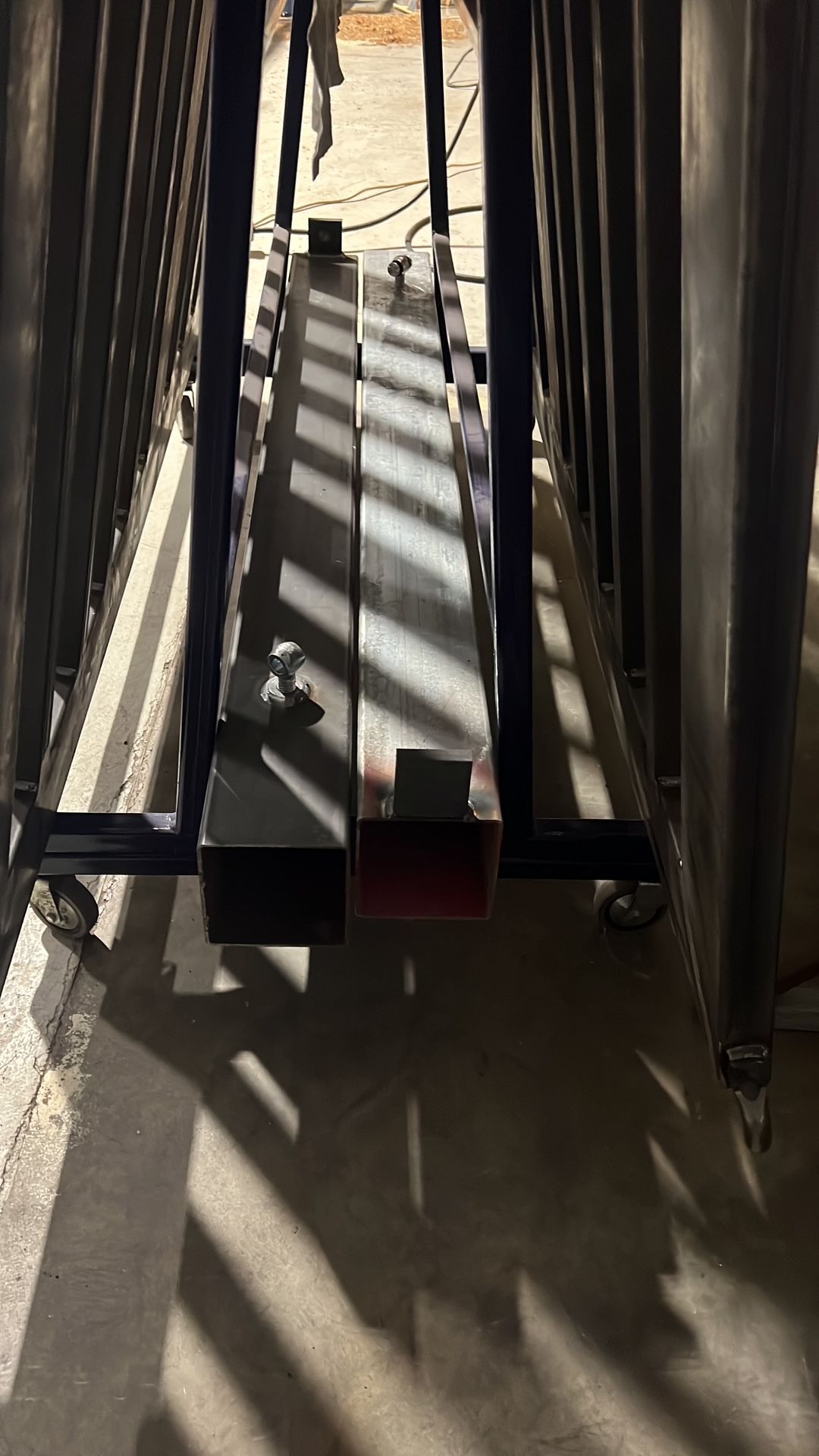 Grandi travi o binari metallici proiettano ombre su un pavimento di cemento illuminato dal sole in un ambiente interno.