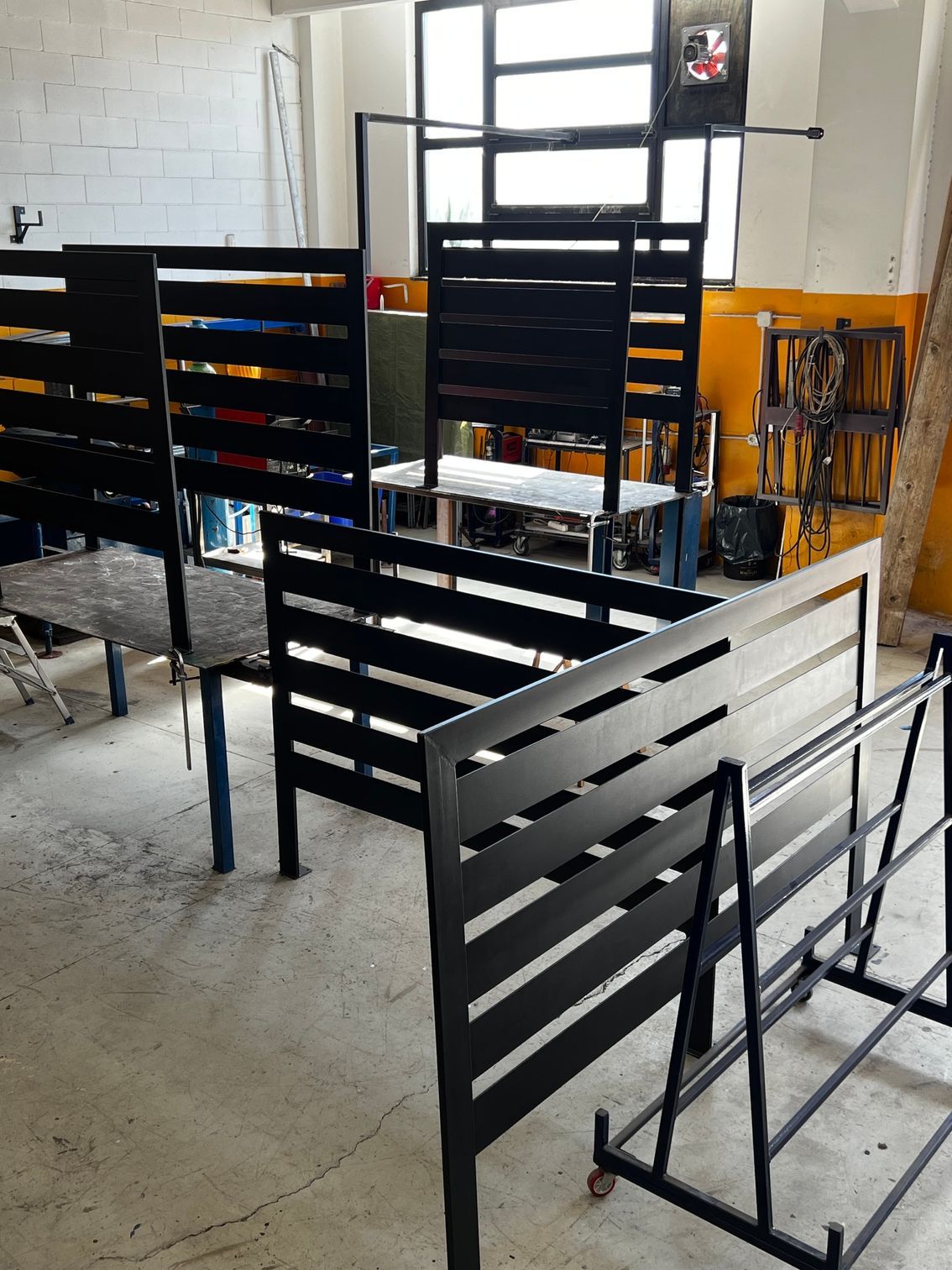 Scaffalature espositive in metallo a doghe nere in un'officina o in un garage con pavimento in cemento e attrezzi sullo sfondo.