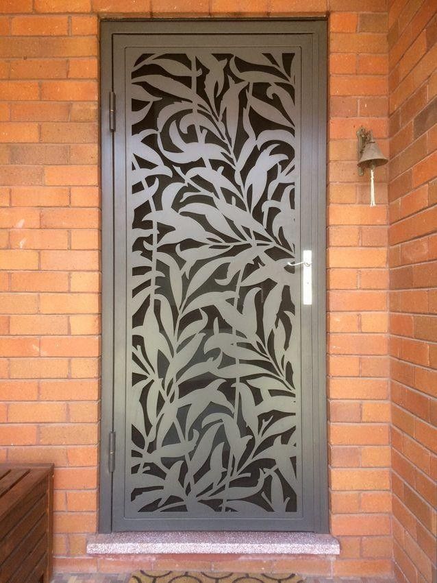 Porta d'ingresso decorativa in metallo grigio con intagli a forma di foglia incastonati in un muro di mattoni.