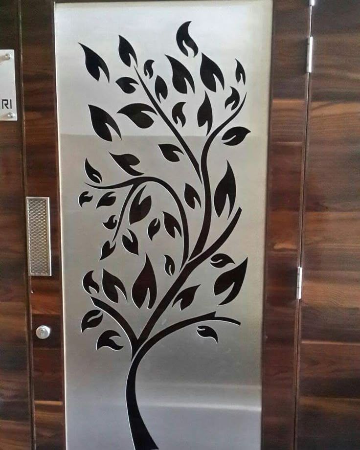Sagoma decorativa di un albero nero su un pannello di vetro satinato con cornice in legno.