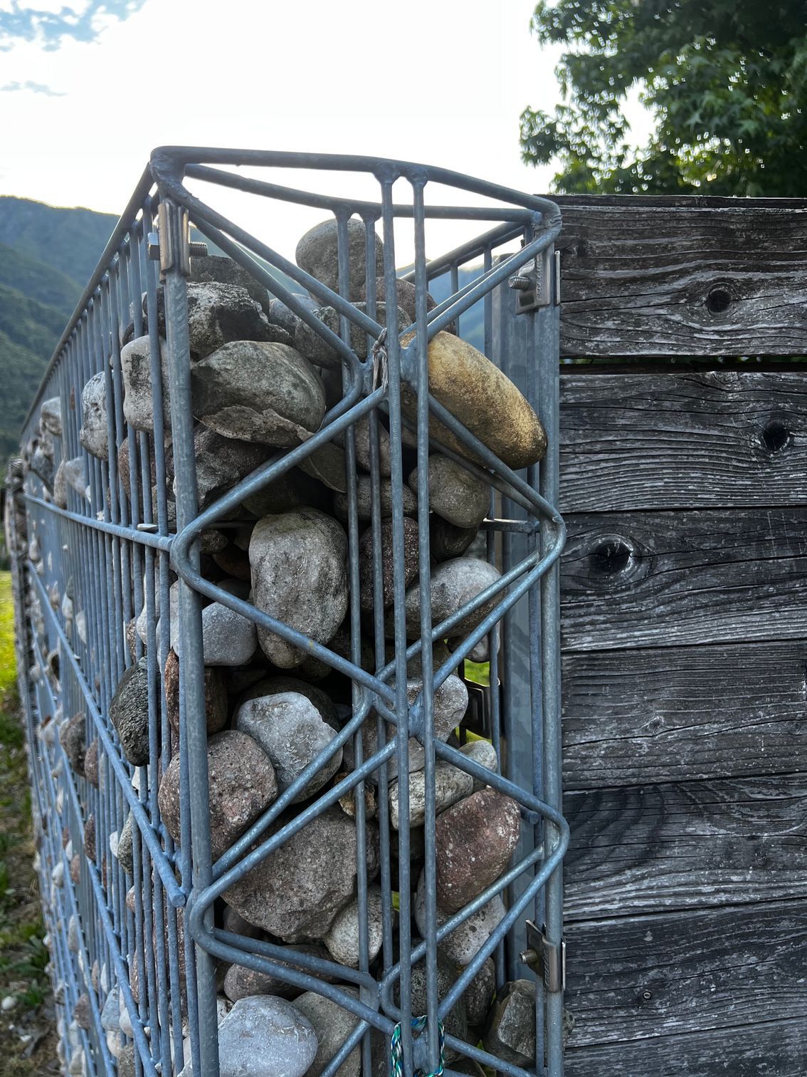 Gabbia di filo metallico riempita di pietre impilate accanto a una recinzione di legno consumata dal tempo all'aperto