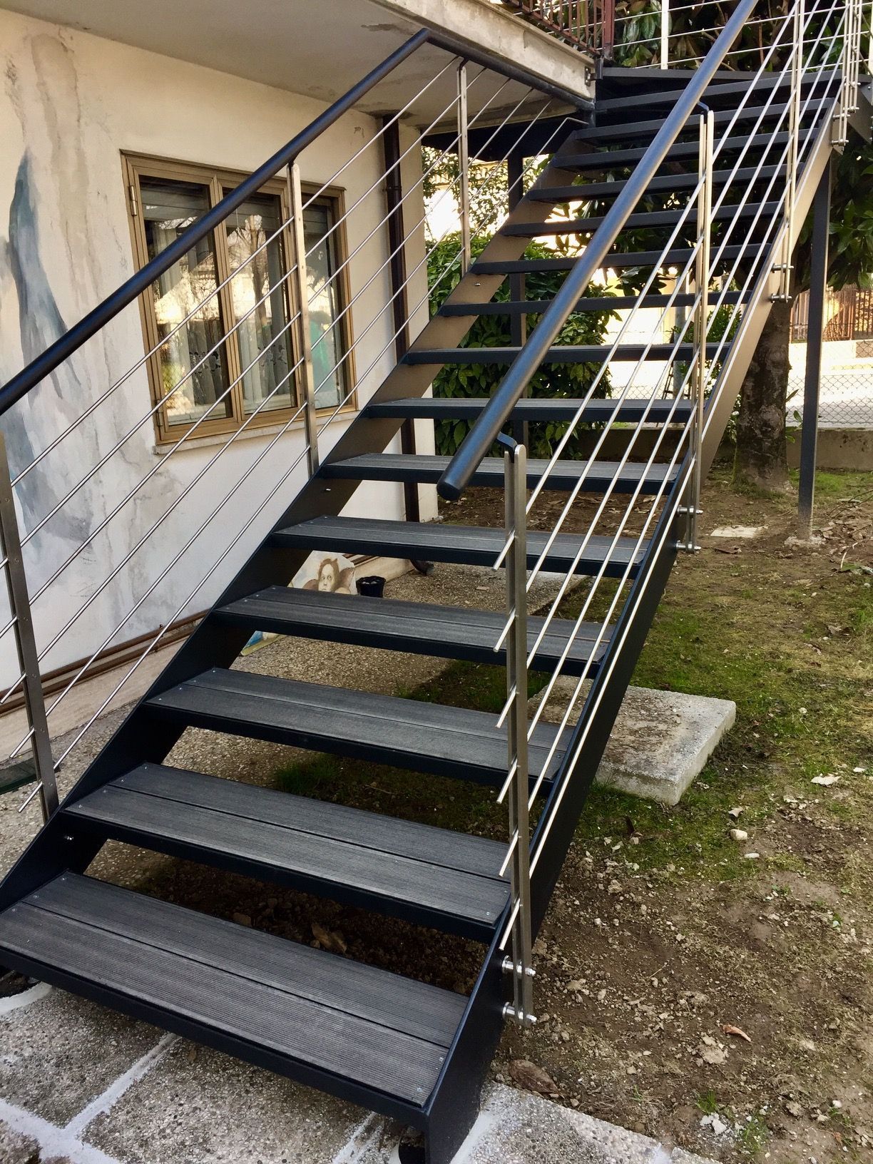 Scala esterna in metallo con ringhiera nera, situata accanto a una casa, che conduce a un ingresso superiore.