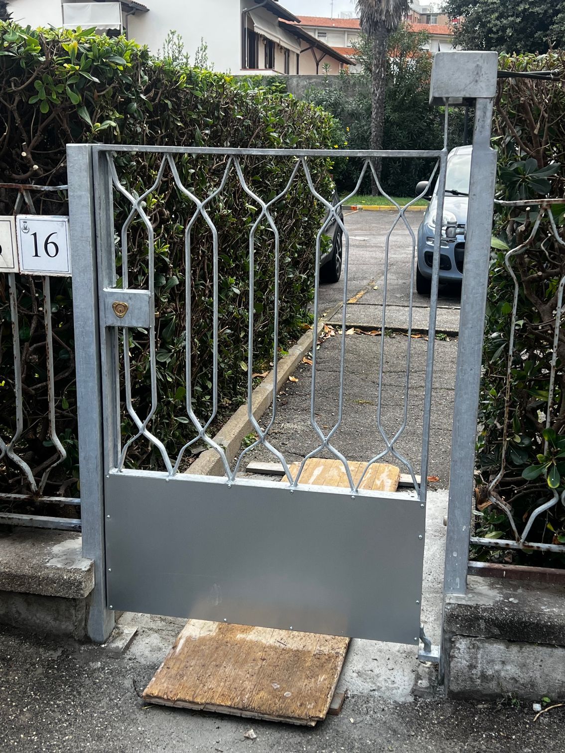 Cancello in metallo grigio con barre decorative all'ingresso di una casa, parzialmente bloccato da un pannello pieno e da uno zerbino a terra.