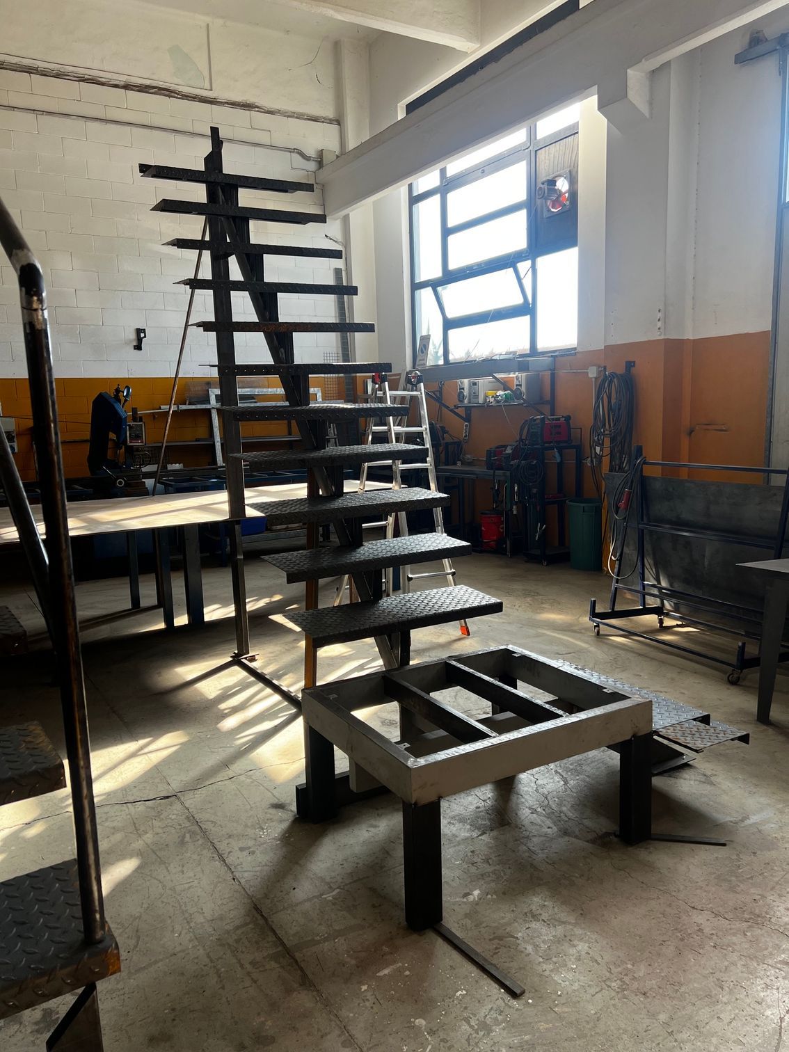 Officina industriale interna con una ripida scala in metallo nero su una piattaforma rialzata vicino alle finestre.