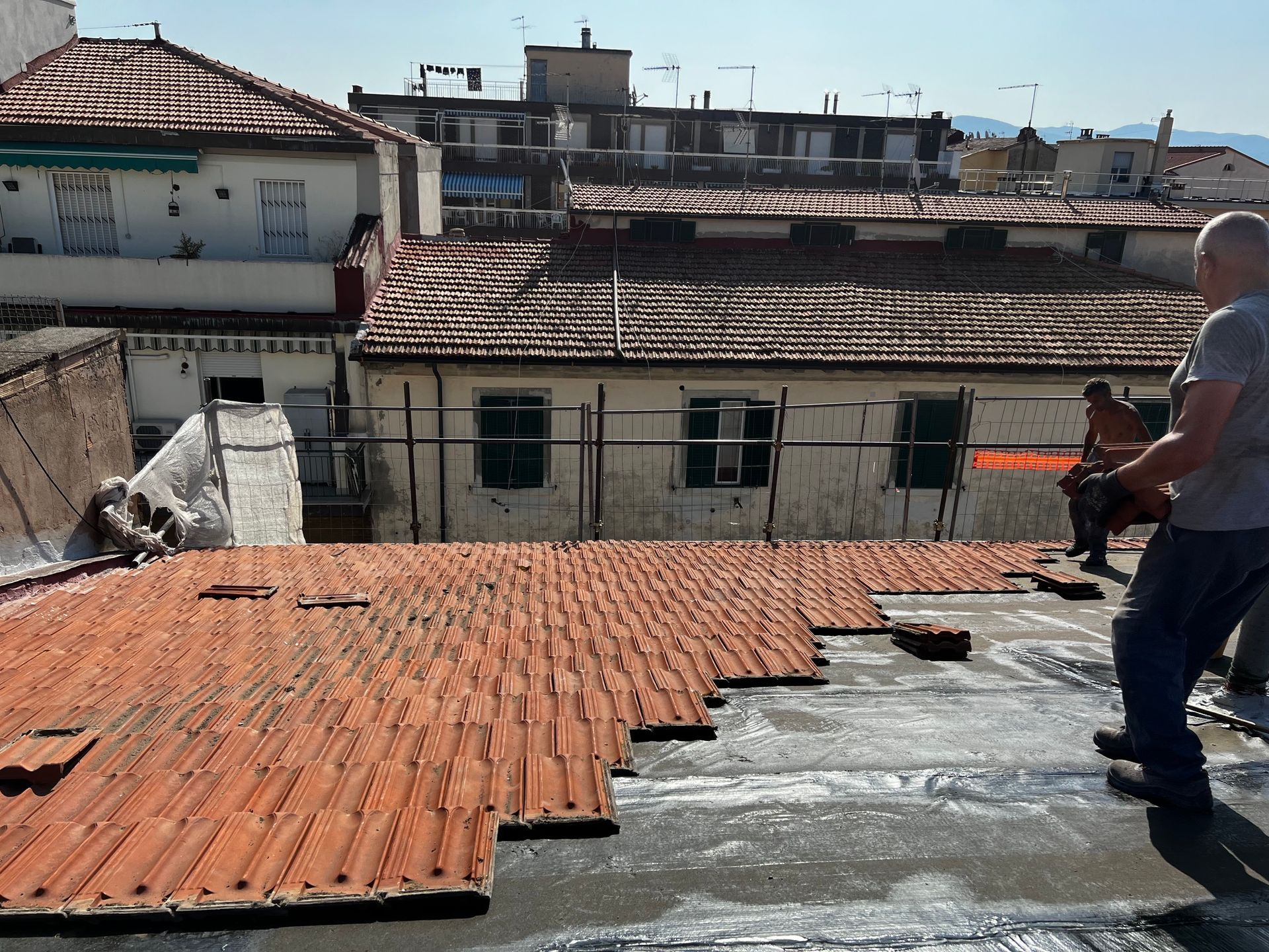 Tetto con tegole rosse consumate dal tempo, un uomo in piedi sulla destra e un panorama urbano sotto un cielo limpido.
