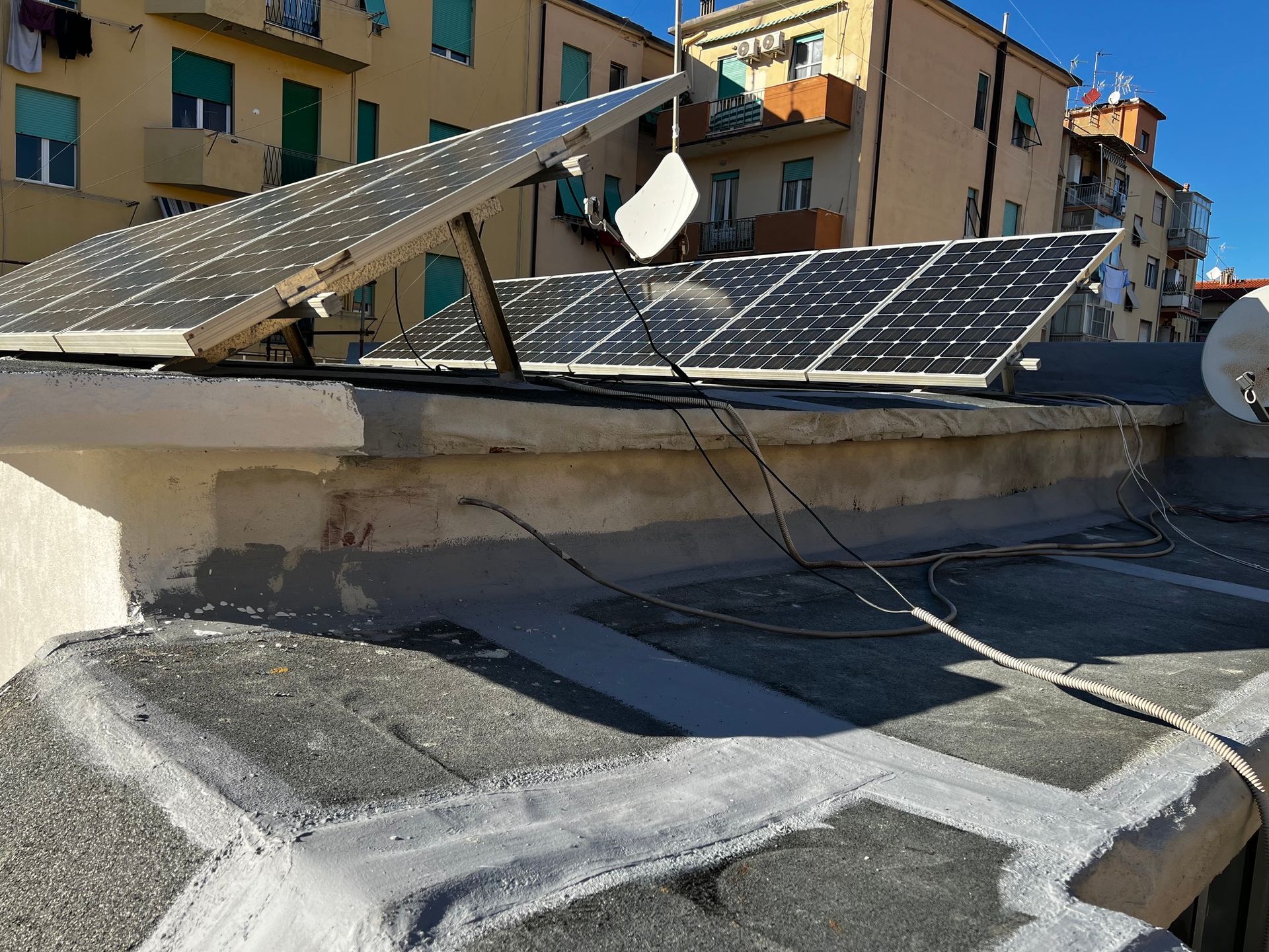 Tetto danneggiato con pannelli solari e struttura metallica piegata su un tetto piano di un edificio.