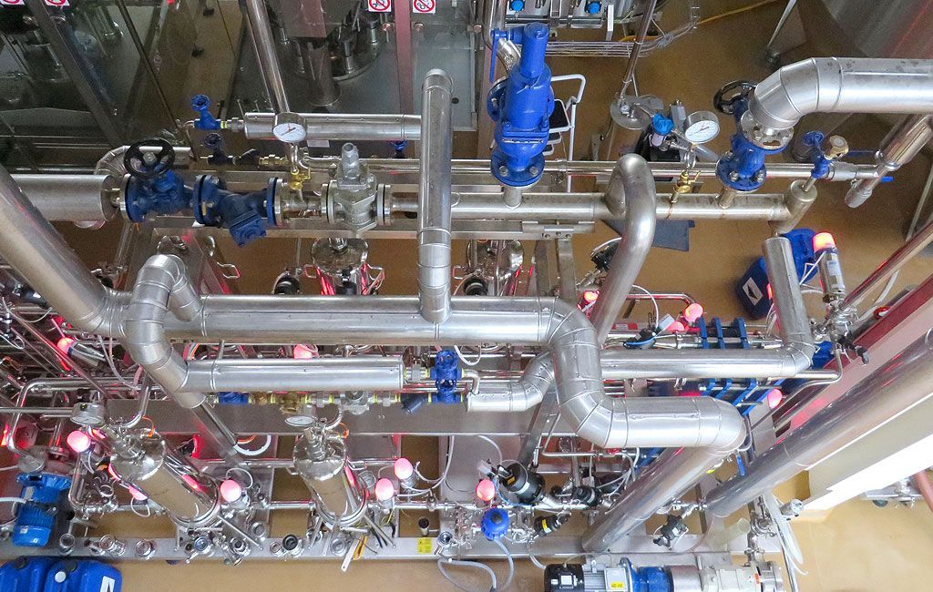 Una fitta rete di tubi argentati lucidi e valvole blu in una sala macchine industriale.