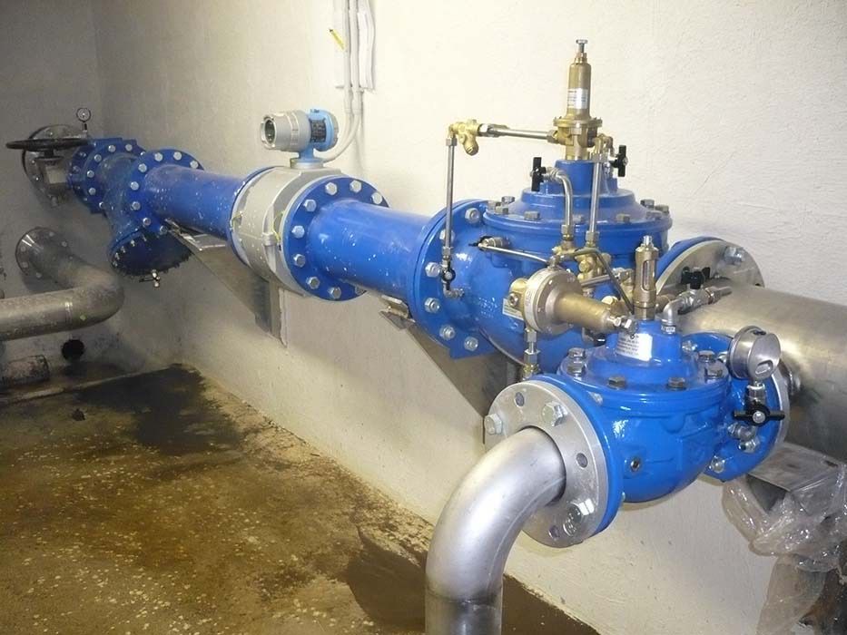 Tubi e valvole industriali blu in un locale tecnico, con acqua sul pavimento.