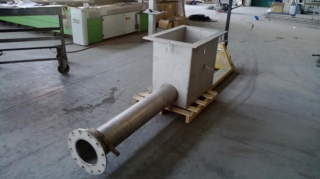 Una grande tramoggia industriale bianca con un lungo tubo metallico appoggiata su un pallet di legno nel pavimento di una fabbrica.