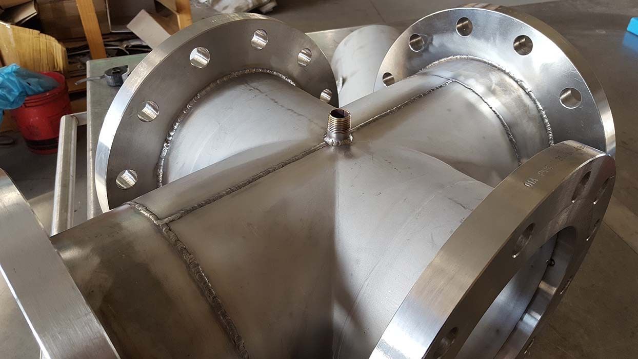 Tubo industriale in acciaio inossidabile con flange imbullonate e giunti saldati sul pavimento di un'officina.