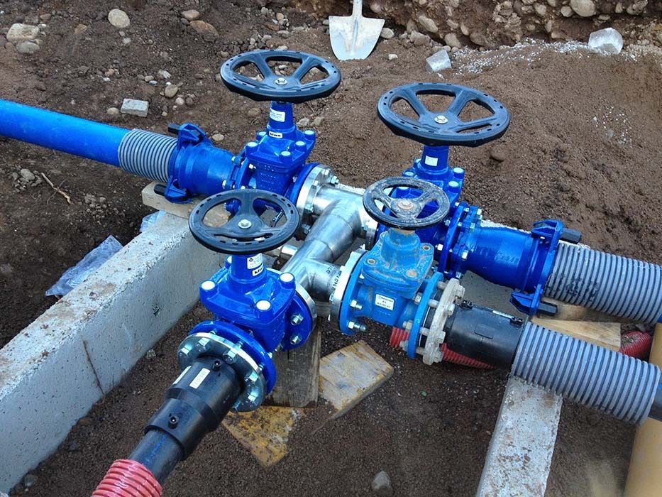 Valvole e tubature industriali blu collegate in una trincea di terra con bordi in cemento.
