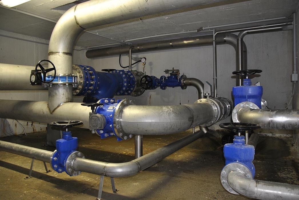 Valvole blu e grandi tubi metallici in un locale tecnico, con tubazioni isolate e raccordi industriali.
