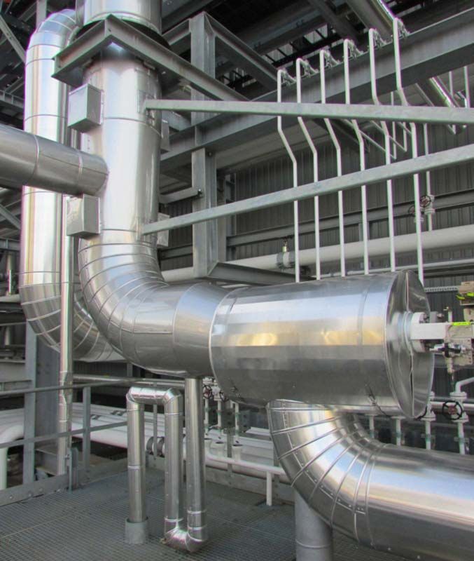 Tubi e condotti industriali color argento lucido all'interno di una fabbrica o di un impianto.