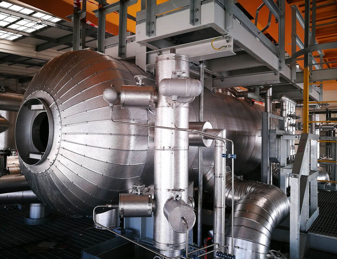 Grande serbatoio metallico industriale e tubature argentate all'interno di una fabbrica o di un impianto di lavorazione.