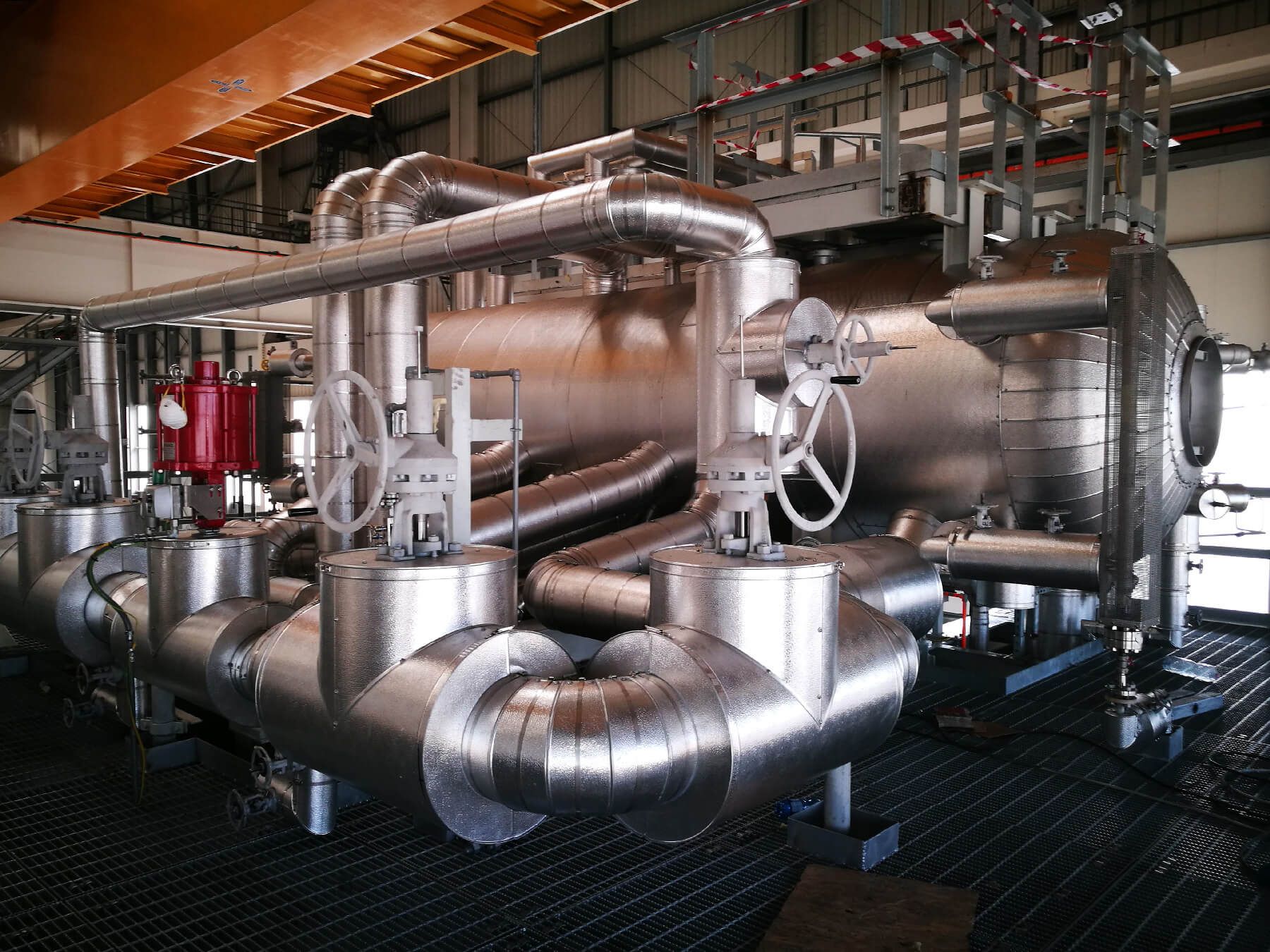 Grande macchinario industriale con tubi e valvole in metallo lucido in un ambiente di fabbrica.