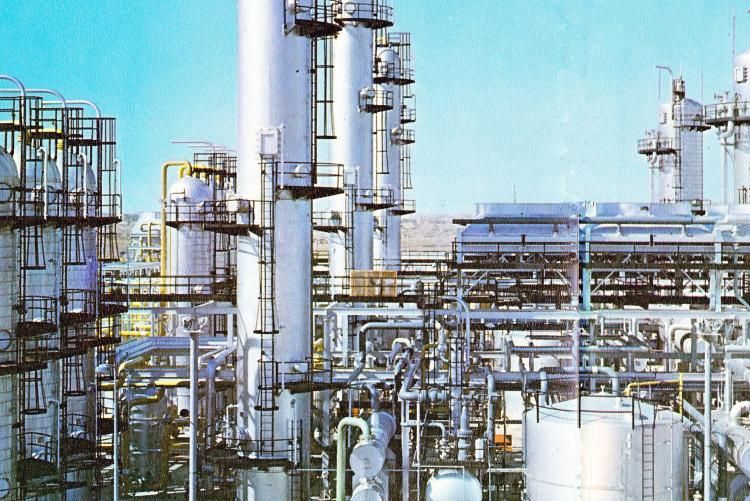 Raffineria industriale con alte tubature e torri metalliche contro un cielo azzurro.