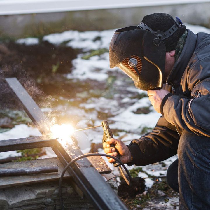 Un uomo sta saldando una struttura metallica all'aperto al crepuscolo, con scintille luminose che volano vicino a un terreno innevato.