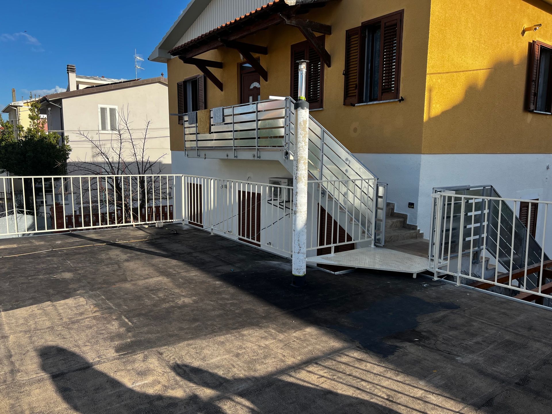 Esterno di una casa gialla con scale e ringhiere bianche che conducono a un portico, con un vialetto pavimentato antistante.