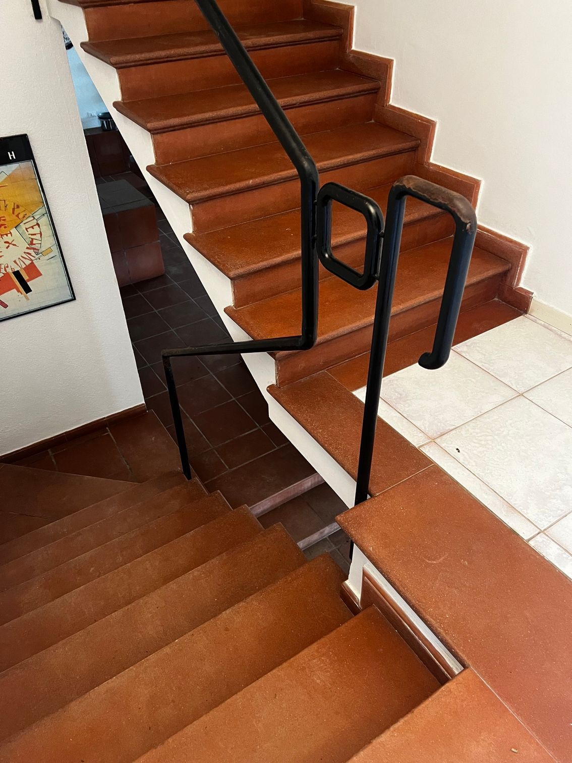 Vano scale con gradini in legno marrone, pianerottolo piastrellato bianco e corrimano in metallo nero.
