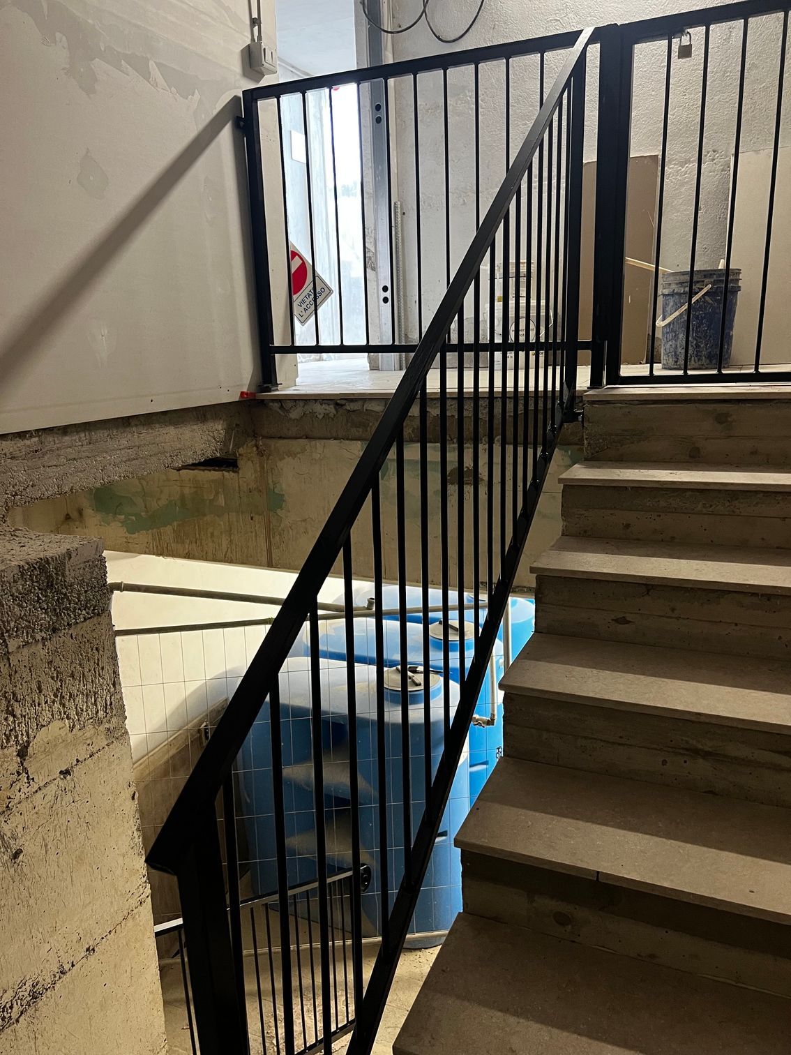 Vano scale con ringhiere in metallo nero, gradini in cemento e un telo blu che copre gli oggetti sottostanti.