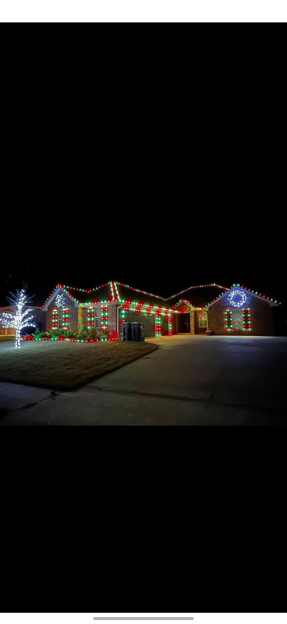 A house at night decorated with colorful, glowing Christmas lights, featuring illuminated rooflines and a lit tree.