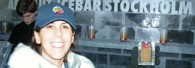 Smiling person in winter hat and white jacket posing at a bar with drinks on shelves behind them