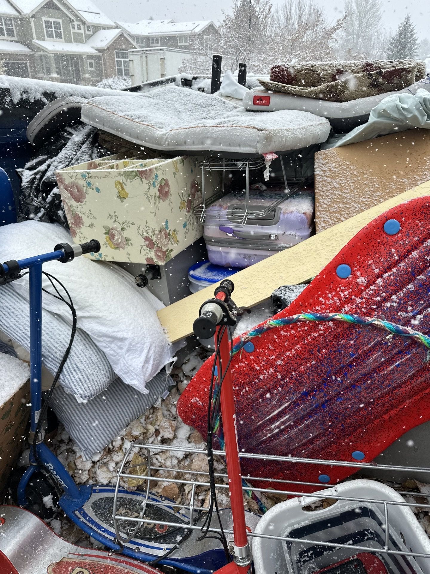 Pile of discarded household items, including a scooter and mattress, covered in snow in Arvada, CO.