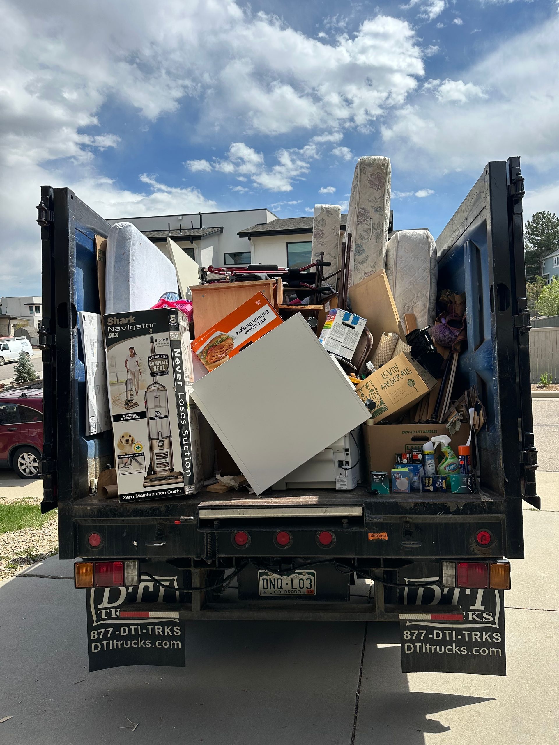 The back of the Colorado Junk Runners truck filled with household items for disposal on a sunny day, parked on a street.