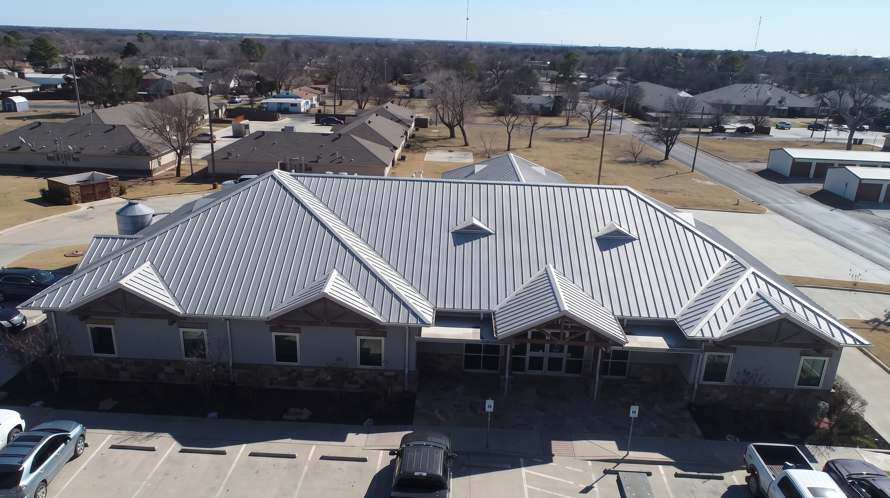 Aerial view of a building with a light gray patterned roof and central entrance in a suburban area.