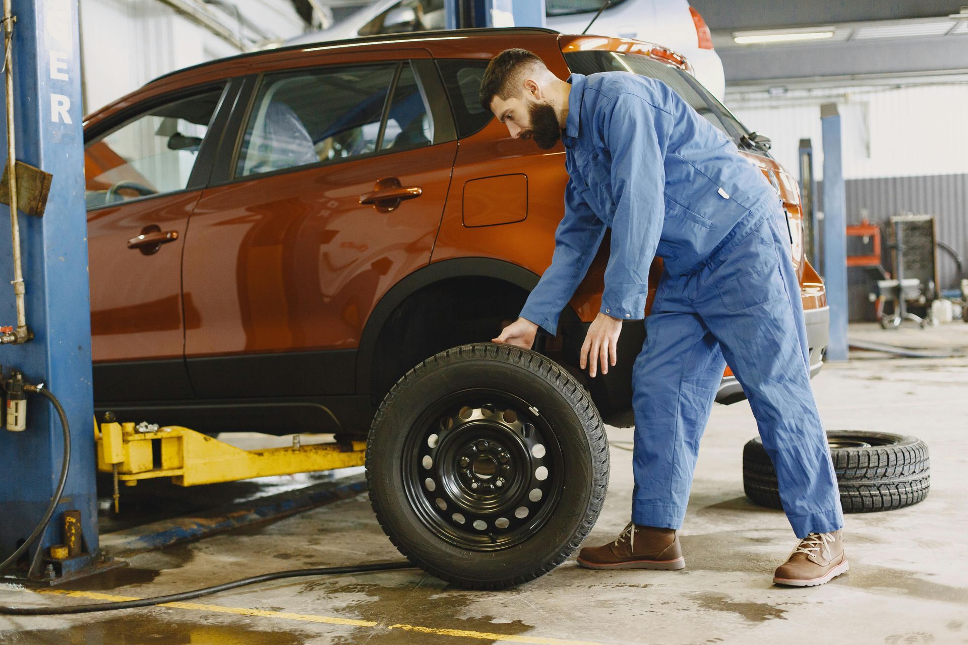 Mechanic in blue overalls changing a car tire in a garage.
