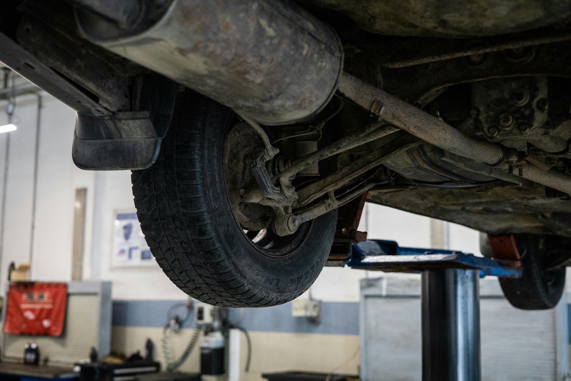 Underside of car with visible exhaust, tire, suspension, and chassis on a lift in a garage.