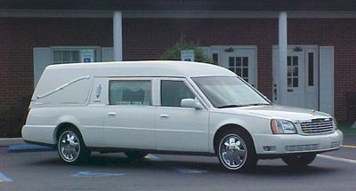 White hearse parked on a street in front of a brick building.