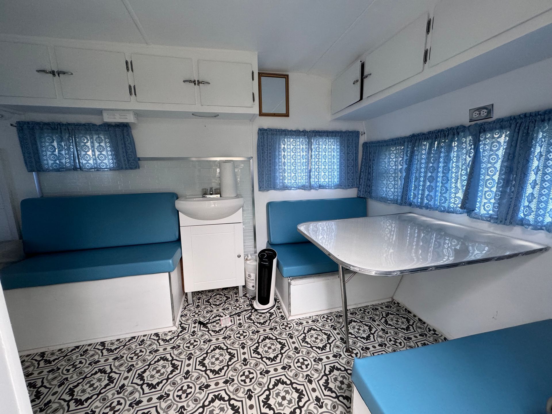 A camper with a table , couch , sink and blue curtains.